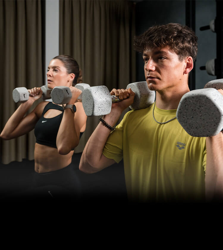 Ragazza e ragazzo che si allenano con i pesi in palestra e sono vestiti con apparel Arena